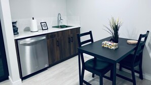 Cozinha compacta com máquina de lavar louça, pia e bancada. Há uma mesa de jantar com cadeiras e um vaso de planta.