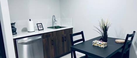 A compact kitchen with a dishwasher, a sink, and a countertop. There is a dining table with chairs and a potted plant.