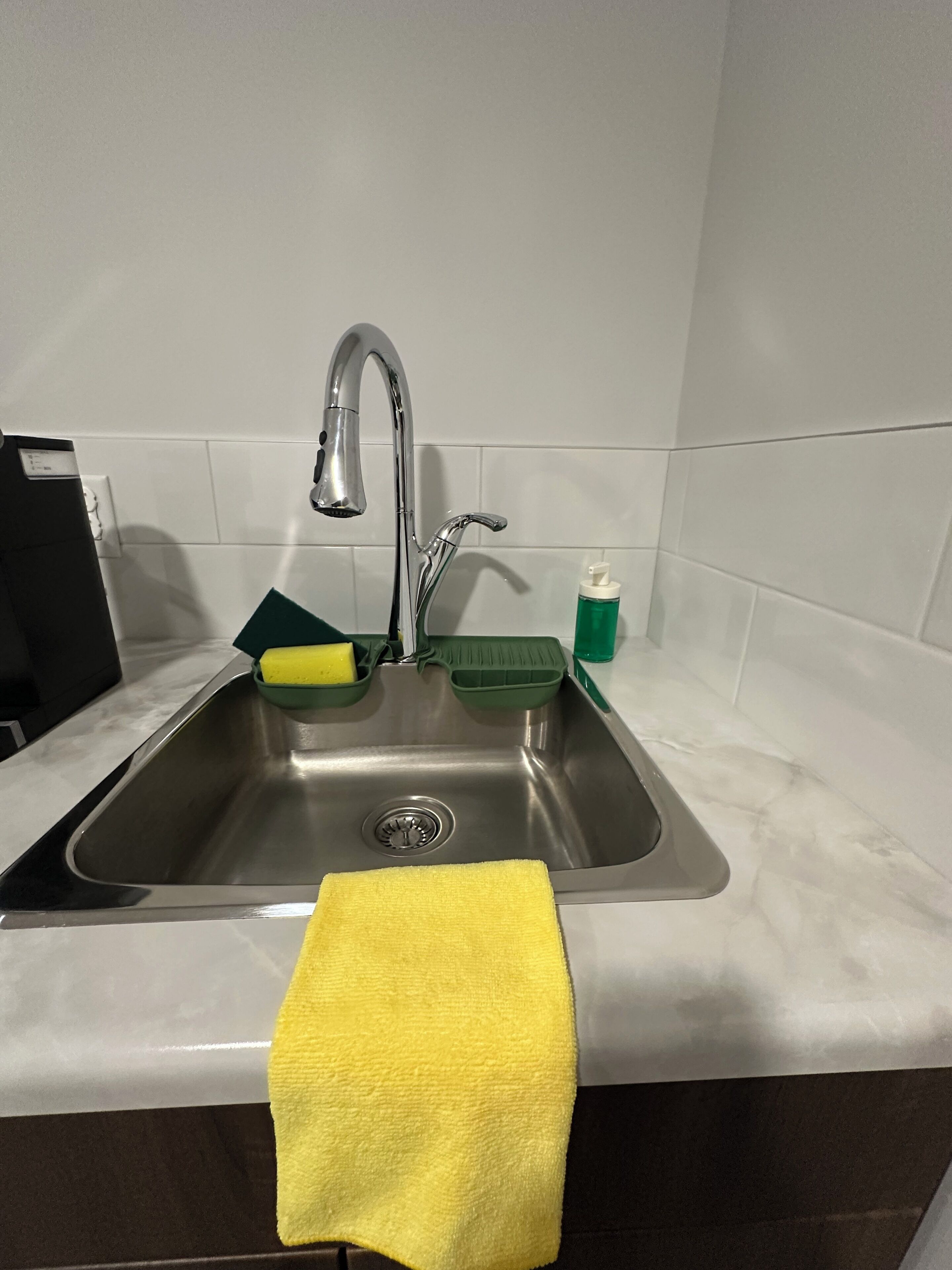 A kitchen sink with a yellow towel, green dish soap, and a yellow sponge.