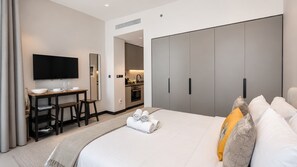 Una habitación de hotel con cama, escritorio, televisión y kitchenette.