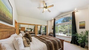 Une chambre spacieuse avec un grand lit, un ventilateur de plafond, une grande fenêtre donnant sur un beau paysage et un miroir.