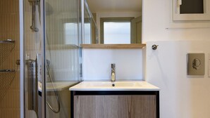 Ein modernes Badezimmer mit Duschkabine aus Glas, einem Holzwaschtisch und einem weißen Waschbecken.