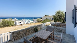 Eine Terrasse mit Holztisch und -stühlen mit Blick auf eine Küstenstadt und das Meer.
