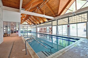 Une piscine intérieure dotée d’un haut plafond en bois, de grandes fenêtres et offrant une vue dégagée sur l’extérieur.