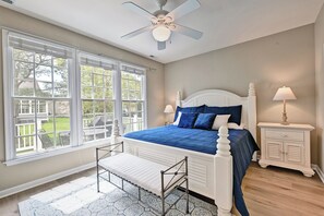 Une chambre à coucher comprenant un lit, un banc, une table de chevet, un ventilateur de plafond et de grandes fenêtres.