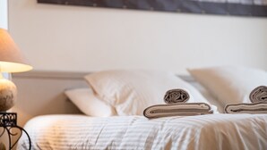 A neatly made bed with rolled towels and a lamp on a bedside table.