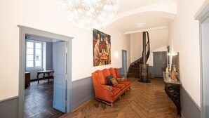 A spacious hallway with a wooden floor, a modern chandelier, a sofa, and a staircase.