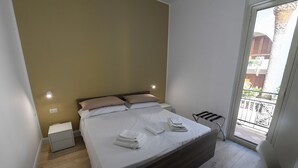 A bedroom with a bed, bedside tables, a small window, and a view of the outside balcony. - Scilla SeaFront Rooms (Scilla)