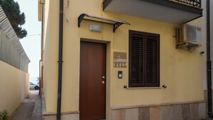 A yellow building with a brown door, a window with blinds, and an air conditioning unit. - Scilla SeaFront Rooms (Scilla)