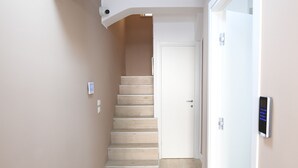 A hallway with a wooden floor, a white door at the end, and a wall-mounted device on the right. - Scilla SeaFront Rooms (Scilla)
