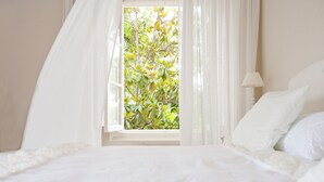 A bedroom with a bed, a window with curtains, and a view of greenery outside. - Suites de Franchy (La Orotava)