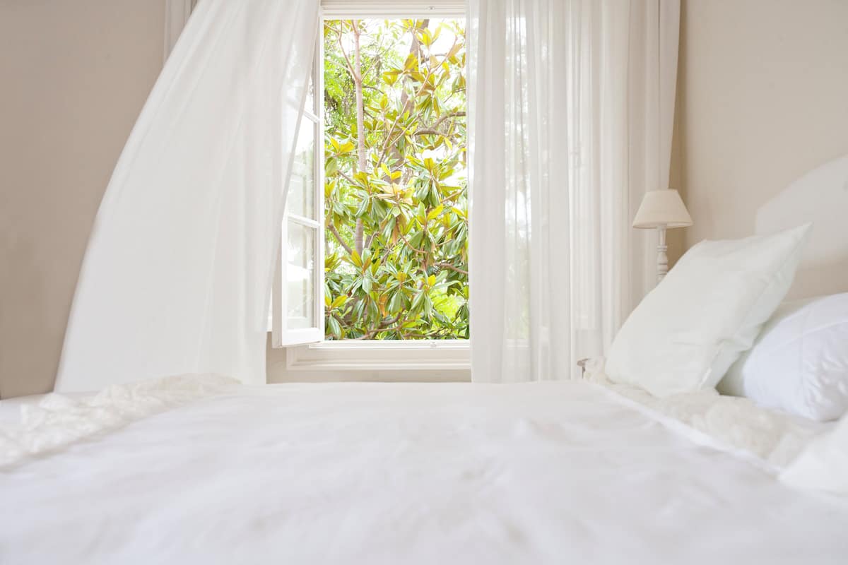 A bedroom with a bed, a window with curtains, and a view of greenery outside.