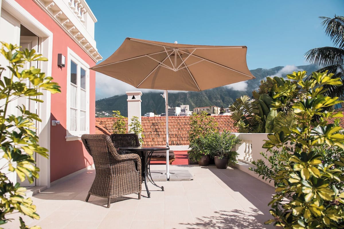 A patio with wicker chairs and a table, a large umbrella, and potted plants.
