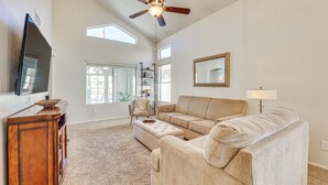 A spacious living room with a large sofa, a television on a wooden cabinet, a ceiling fan, and a bookshelf. - Swim w/ a View: Scenic Desert Retreat in Glendale (Glendale)