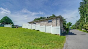 Un bâtiment d’un seul étage, construit en briques, avec une clôture blanche, un petit garage attenant et une allée pavée.