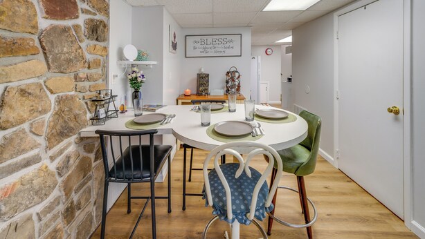 Un coin repas avec un mur en pierre, une table ronde dressée pour quatre personnes et une chaise verte.