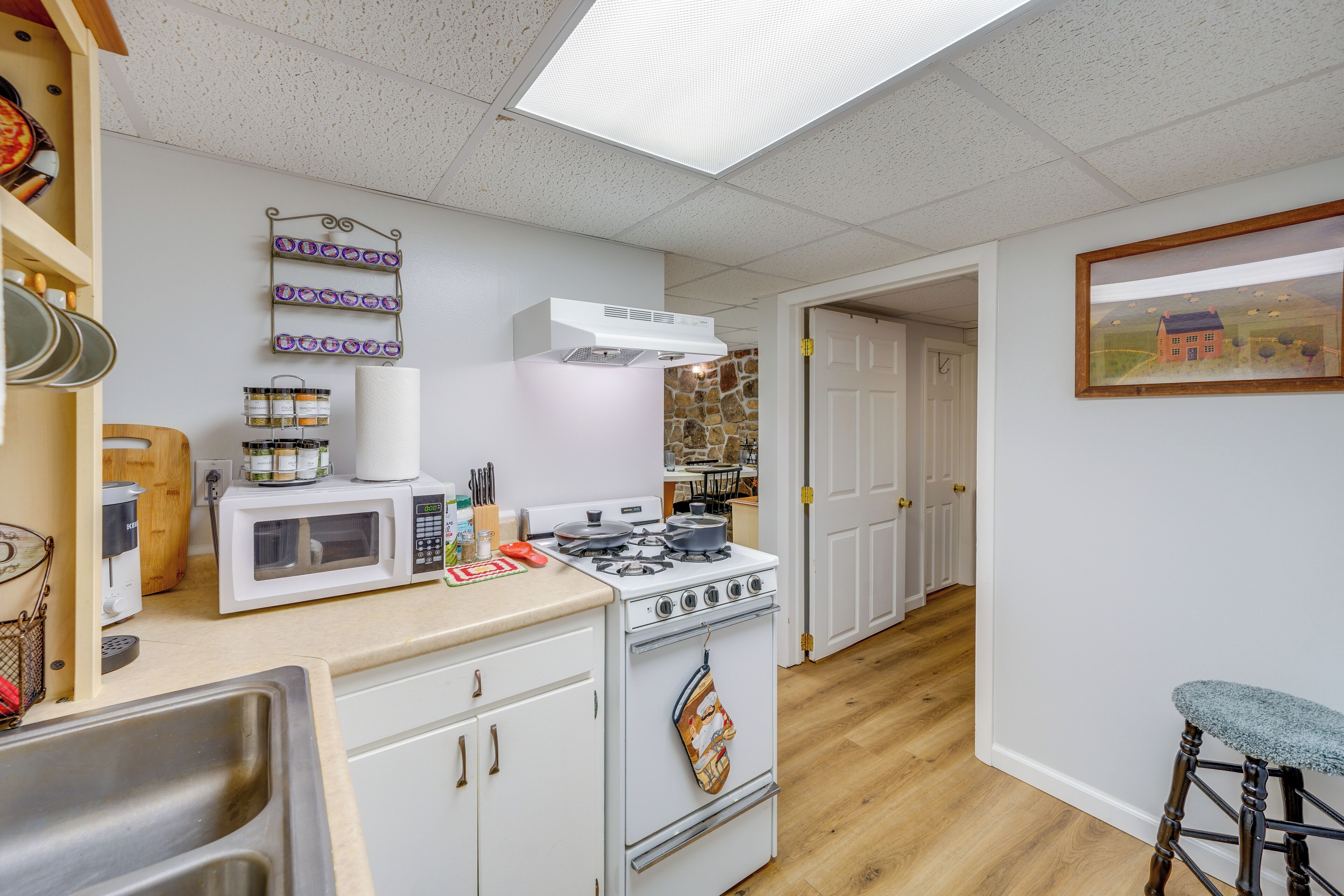 A kitchen with white cabinets, a stove, a microwave, and a hanging pot rack.