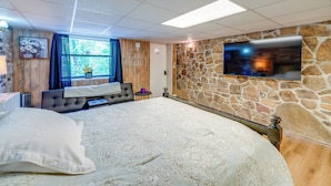 Une chambre avec un grand lit, un mur décoratif en pierre, un téléviseur fixé au mur et une fenêtre avec des rideaux.