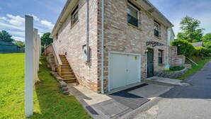 Une maison à deux étages, construite en briques, avec une porte de garage à l’avant, un petit porche et un escalier menant à l’entrée.