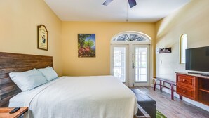 Un dormitorio con cama, ventilador de techo, televisor, banca y puerta con vistas.