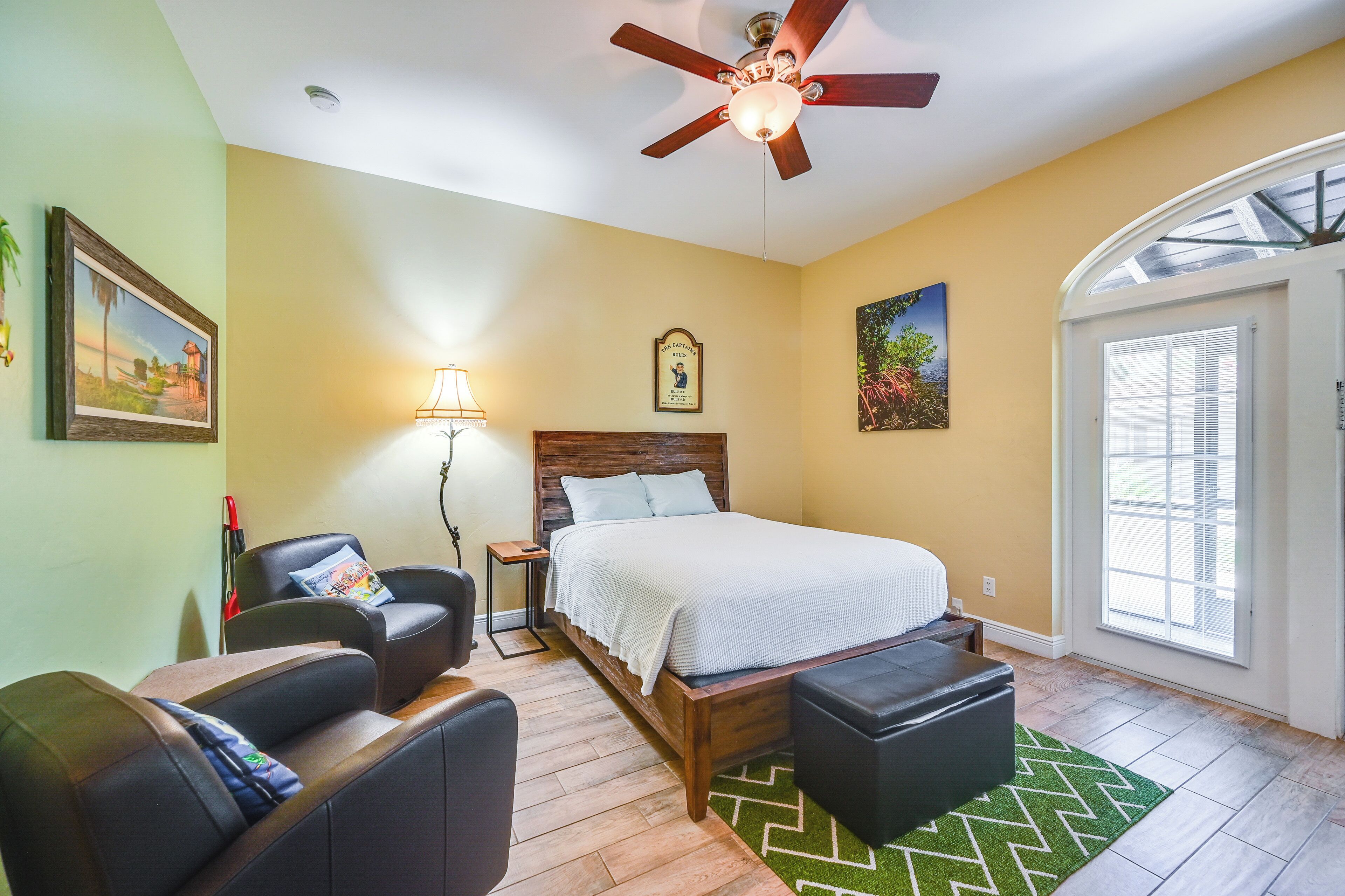 A bedroom with a bed, a nightstand, a chair, a desk, a ceiling fan, and a window.
