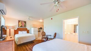 Ein Hotelzimmer mit zwei Betten, einem Schreibtisch, einem Stuhl, einem Deckenventilator und einer Küchenzeile.