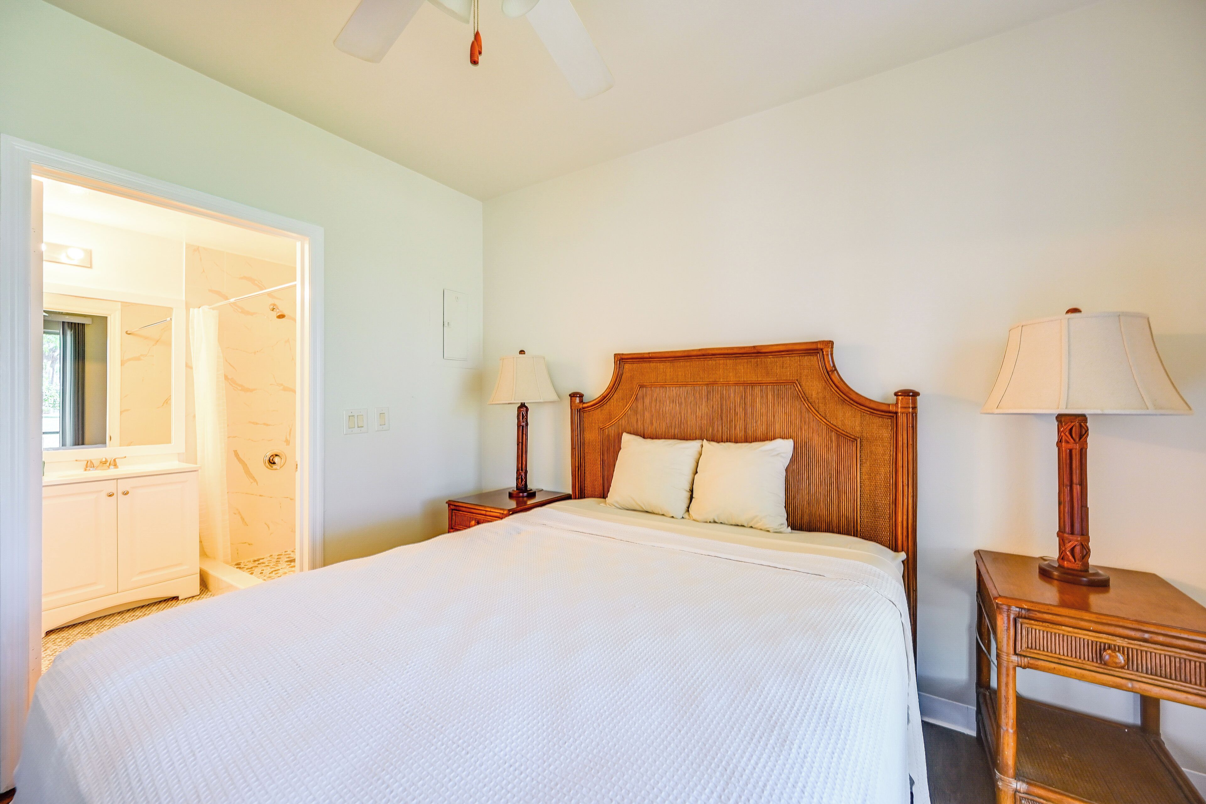 A hotel room with a large bed, wooden headboard, two bedside tables with lamps, a wardrobe, and a ceiling fan.