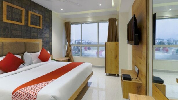 A hotel room with a large bed, a TV, a desk, and a view of the city. - Hotel Rose Gold (Vadodara)