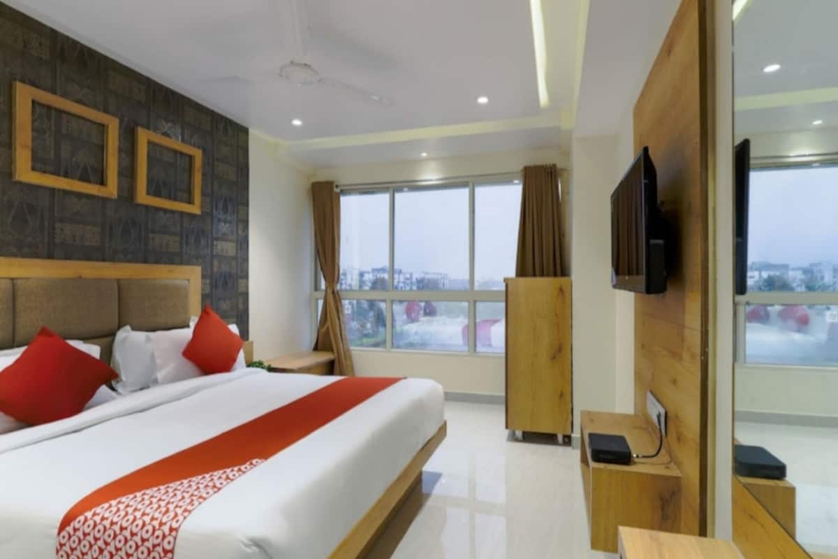 Ein Hotelzimmer mit einem großen Bett, einem Fernseher, einem Schreibtisch und Blick auf die Stadt.