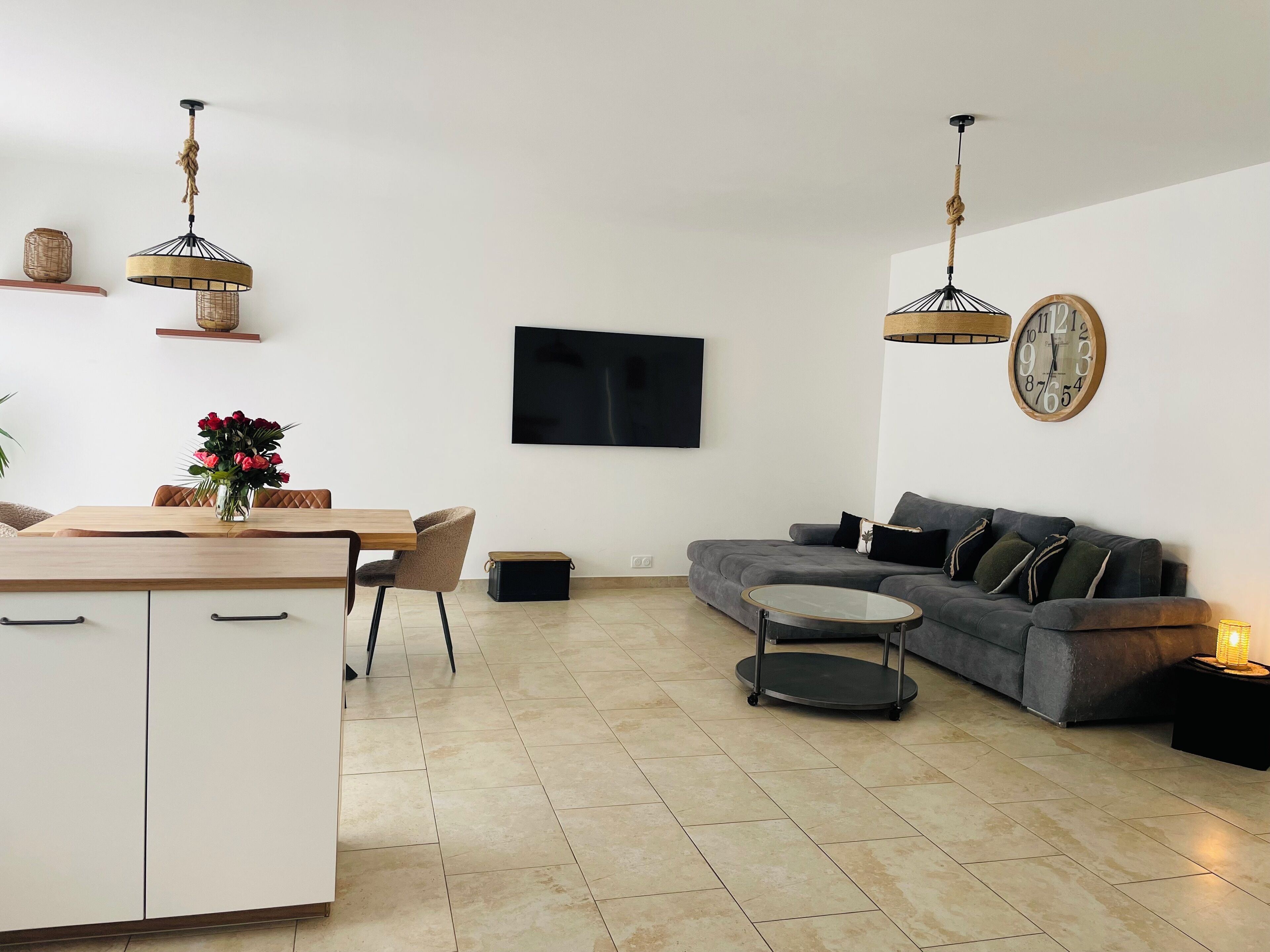 Un soggiorno moderno con un divano grigio, un tavolo da pranzo in legno con sedie, una TV a parete e un tavolino rotondo.