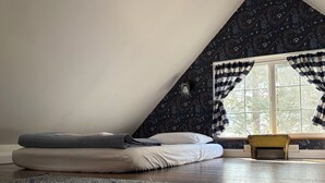 A bedroom with a sloped ceiling, a bed with pillows, a rug, and a window with curtains. - Peace & Simplicity in a Little Red Cabin on the Farm (Lena)