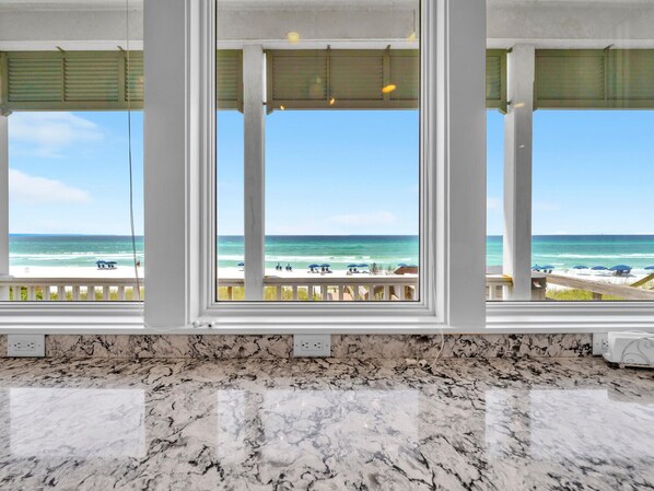 A kitchen with a marble countertop and a view of the beach through large windows.