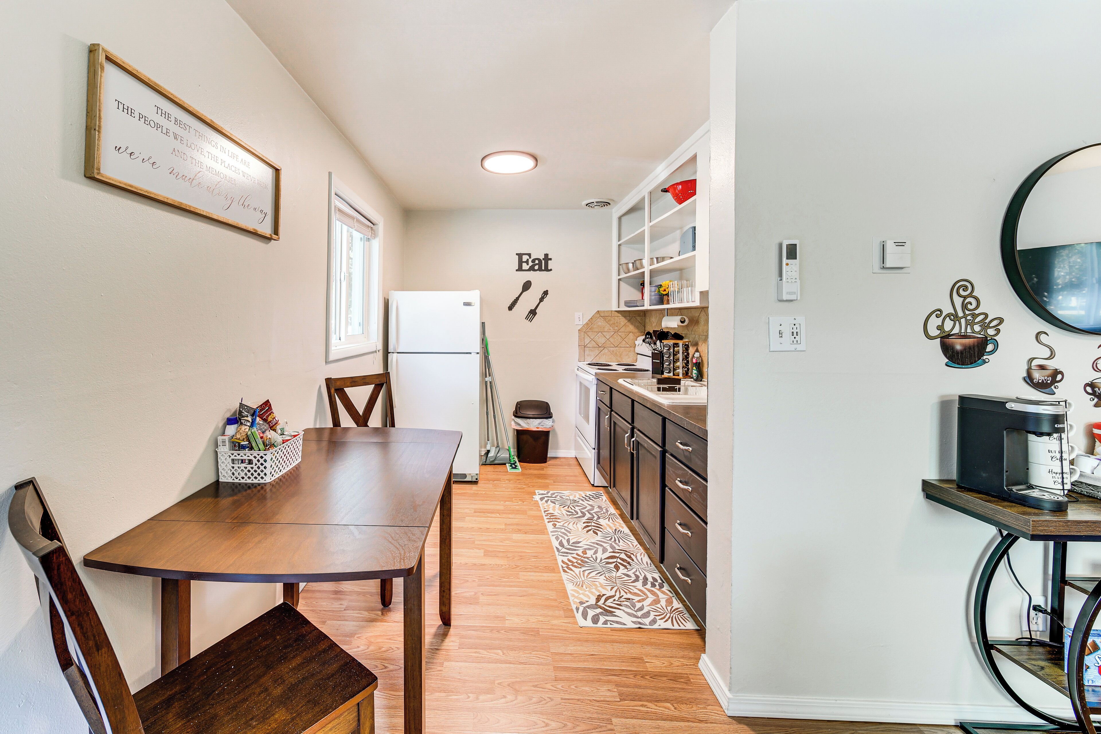 A compact kitchen with a dining table, chairs, a refrigerator, and a coffee machine.