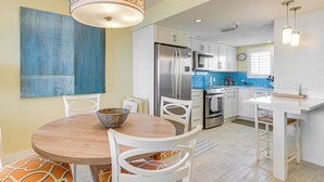 A modern kitchen with white cabinetry, stainless steel appliances, and a round wooden dining table with white chairs. - Gulf-view Condo w/ Beach Access in Hudson (Hudson)