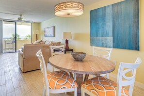 A dining area with a round wooden table, white chairs with orange cushions, a woven basket, and a wall-mounted lamp. - Gulf-view Condo w/ Beach Access in Hudson (Hudson)
