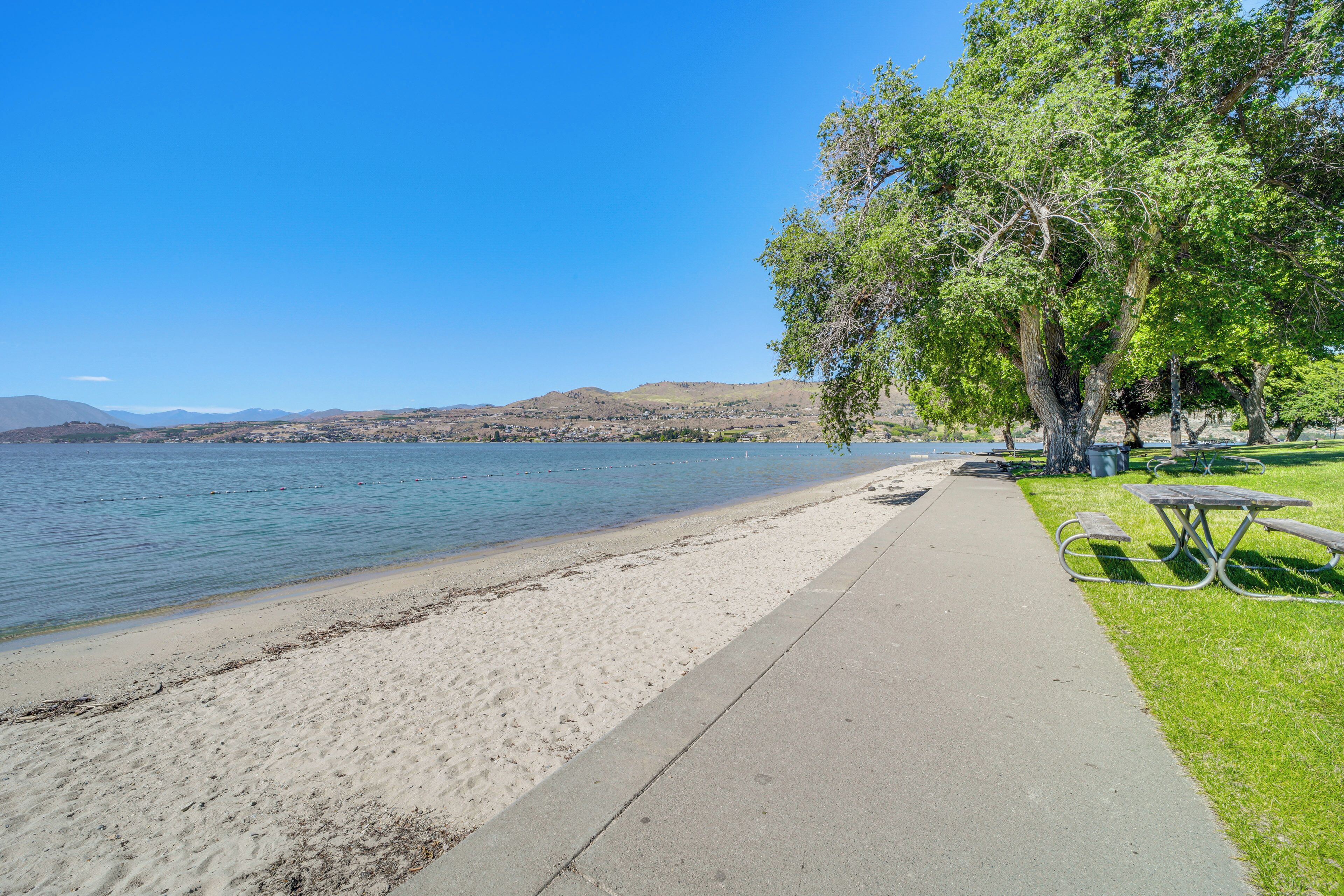 Un parc au bord du lac, doté d’une promenade dallée, de tables de pique-nique et d’arbres.