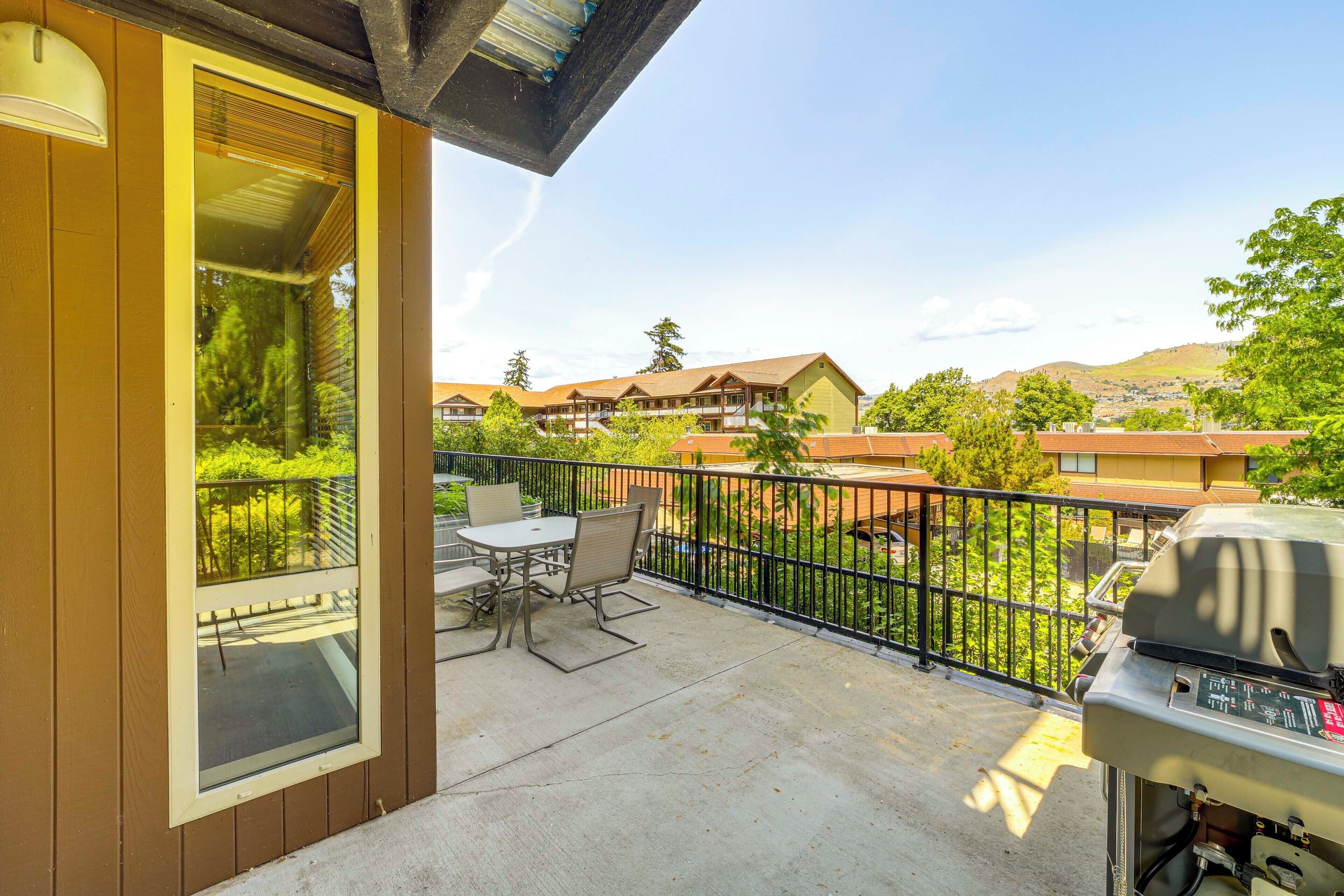 Un balcon avec une table et des chaises, un barbecue et une vue sur les bâtiments environnants.
