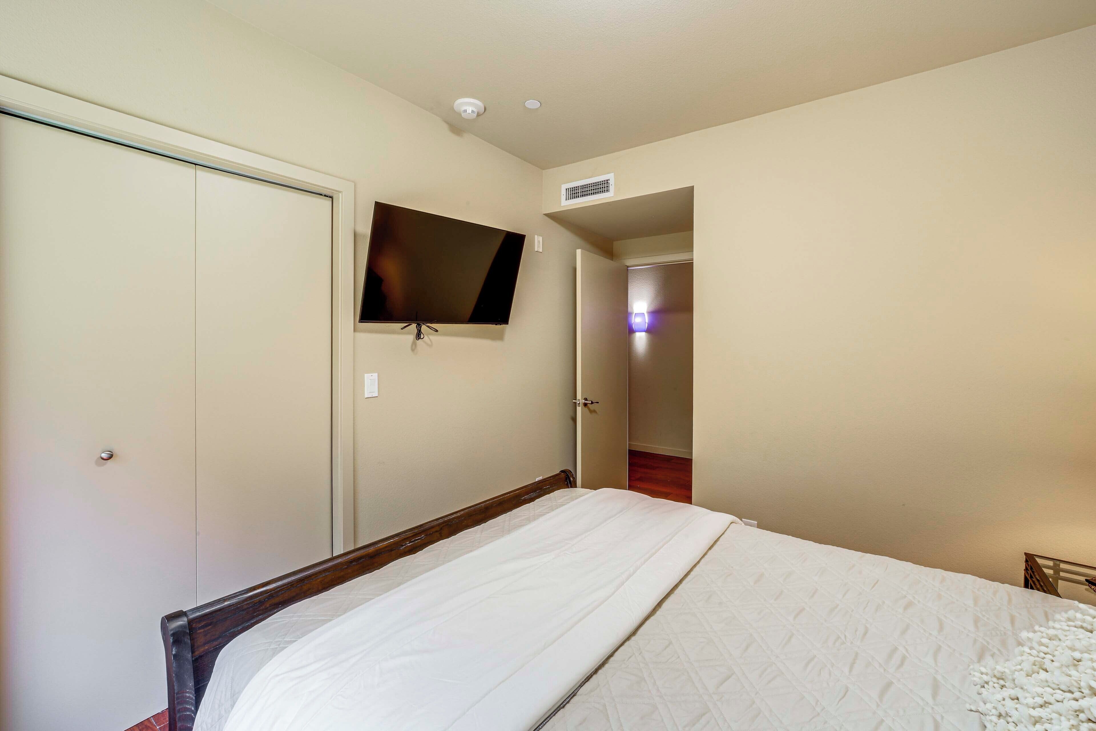 Un dormitorio con cama, televisor montado en la pared y una puerta que da a otra habitación.