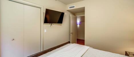 Un dormitorio con cama, televisor montado en la pared y una puerta que da a otra habitación.