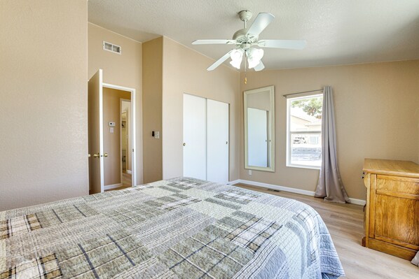 Um quarto com uma cama, um ventilador de teto, um armário de madeira, uma porta e uma janela com cortinas.