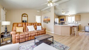 A spacious living room with a leather sofa, a coffee table, and a kitchen area with wooden cabinets and a bar stool. - 6 Mi to Downtown Pahrump: Scenic Desert Retreat (Pahrump)