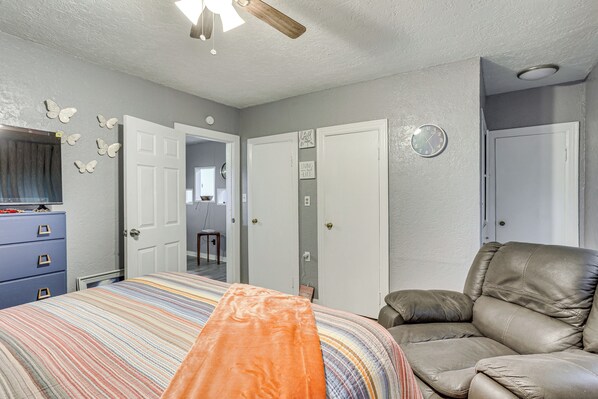 Un dormitorio con una cama, un sillón de cuero, un aparador y una puerta que da a otra habitación.