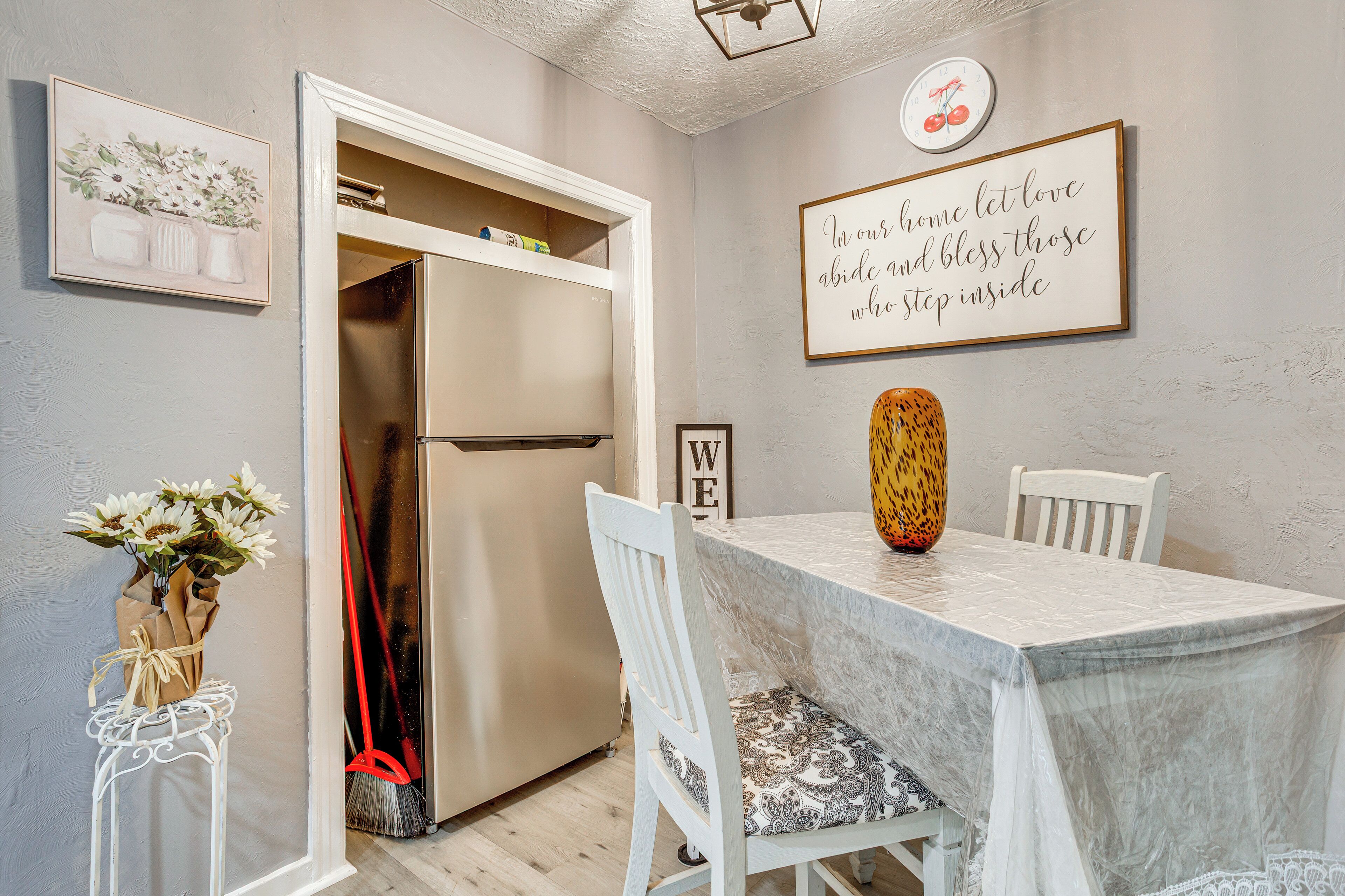 A dining area with a marble table, white chairs, a vase with flowers, and a refrigerator in the background.
