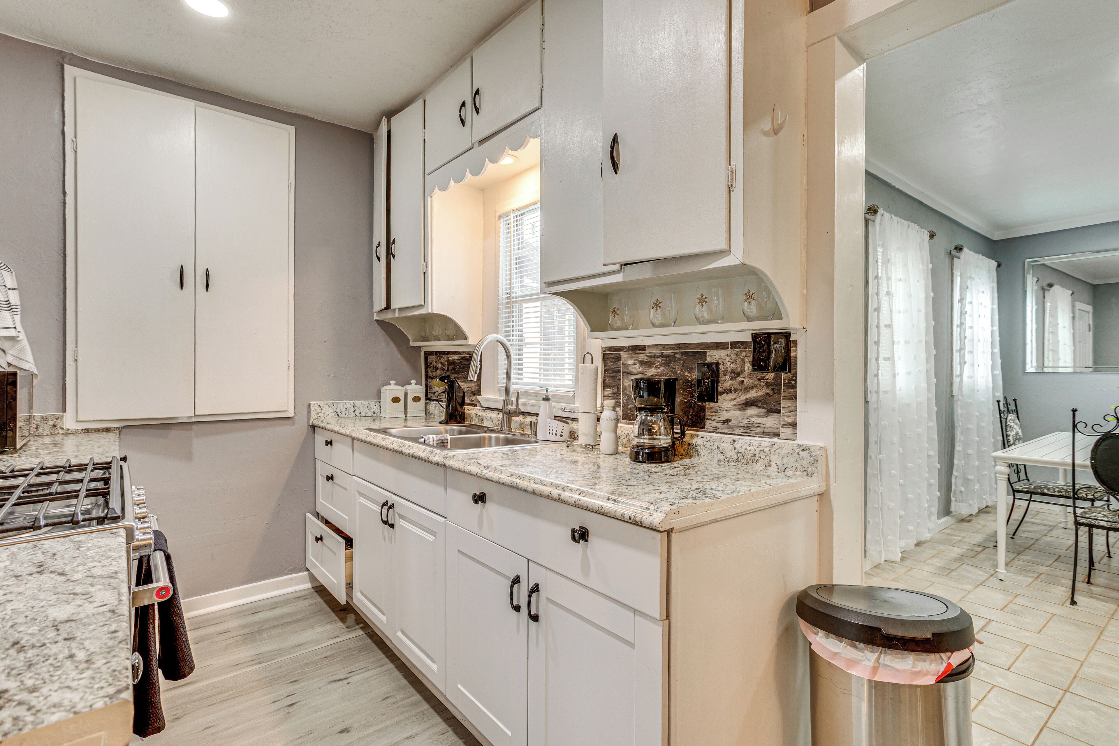 A kitchen with white cabinets, a granite countertop, a stove, and a trash can.