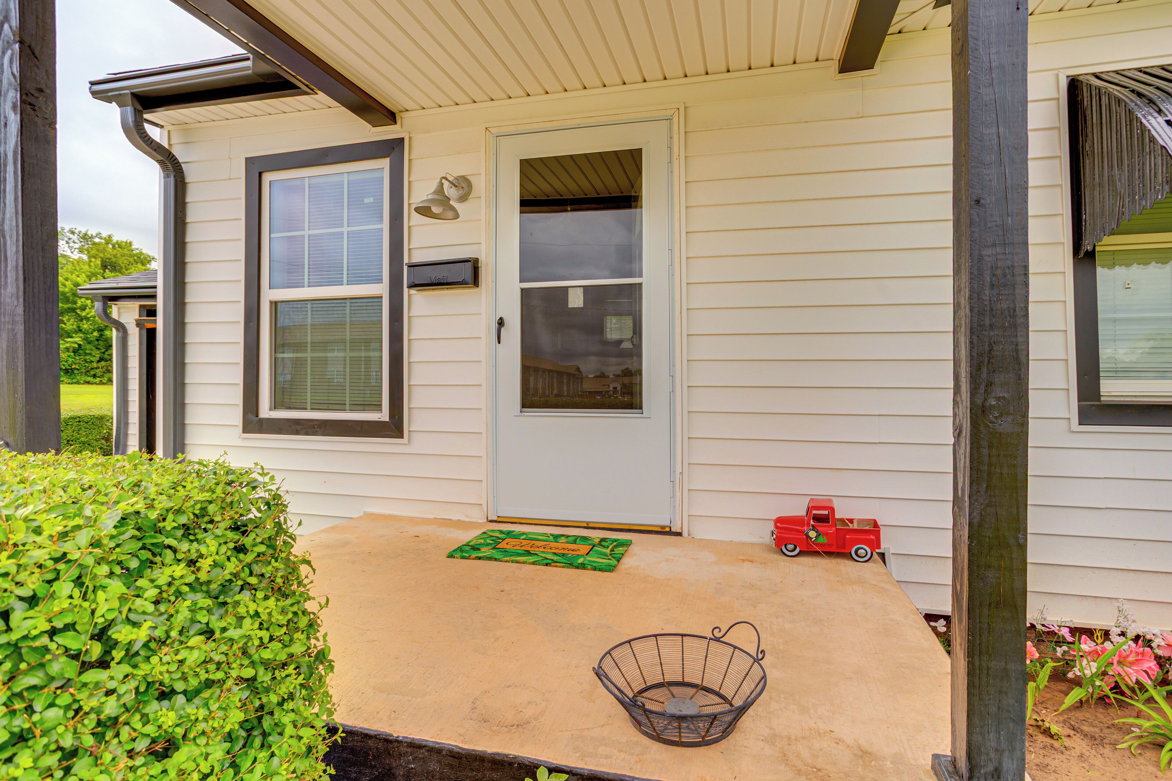 A house with a front porch, a door, a window, a small red toy truck, and a metal basket.
