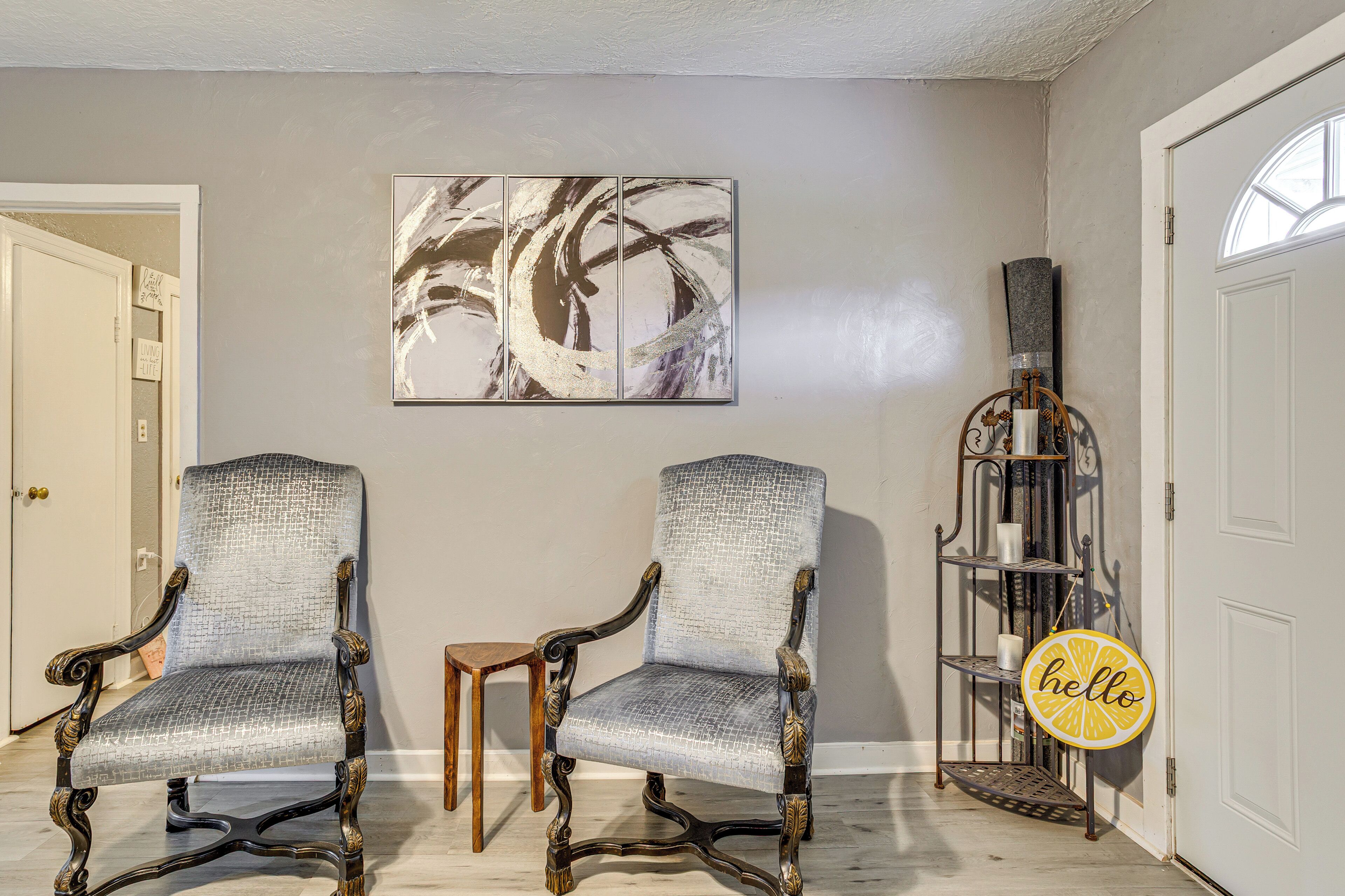 A room with two upholstered chairs, a small table, a wall-mounted shelf with decorative items, and a door.