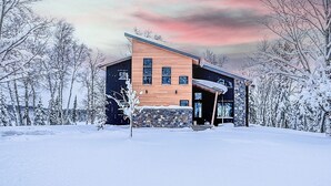 Moderni talo, jossa on kivinen pohjarakenne, puinen yläosa ja suuri lasiovi.