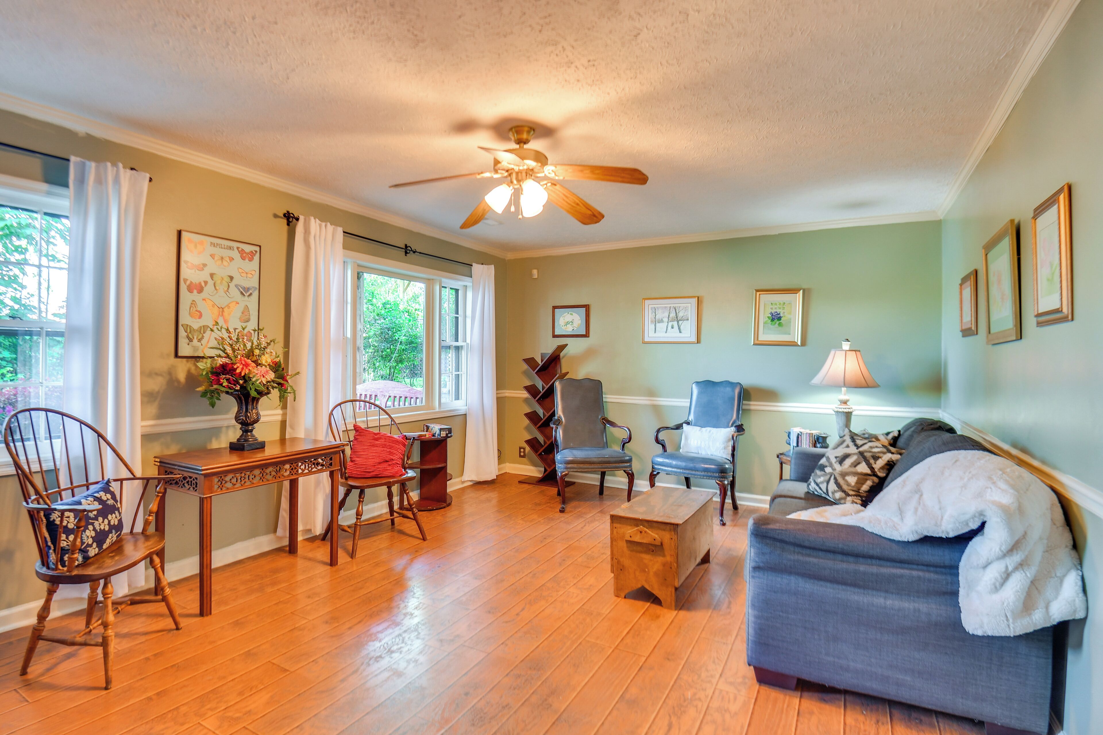 A living room with hardwood floors, a ceiling fan, a sofa, two armchairs, a coffee table, and a side table with a lamp.