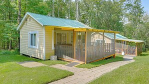A small, single-story cabin with a covered porch and a fenced deck area. - Screened Porch + Fire Pit: Cabin Near Bethel Woods (Mongaup Valley)