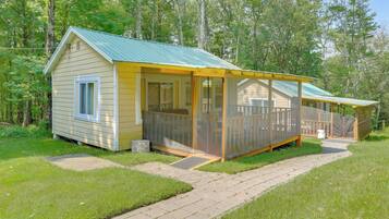 A small, single-story cabin with a covered porch and a fenced deck area.